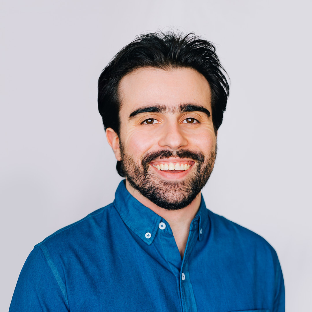 a portrait of a man smiling, with black hair and a beard